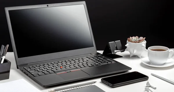 Desktop with laptop pc smart phone, notepads office suppliers headphones. Home Office laptop screen blank template display workspace. Work desk table on black background. Long web banner.