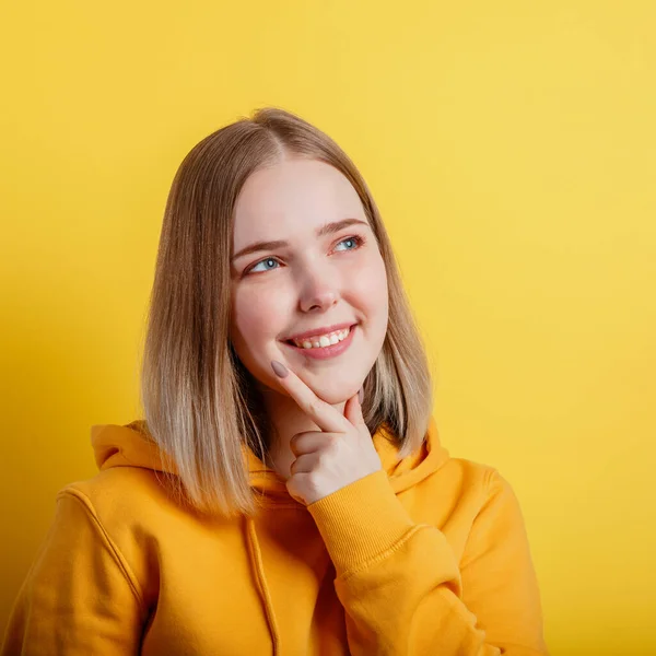 Happy smiling young woman think thought. Portrait of emotional teenage girl thinking about idea or positive question on color yellow background. Square.