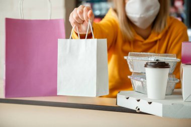 Paket yemek kağıdı maketi. Yiyecek kutusu hazır kahve içer ve restorana gider. Mutfak çalışanı internetten eldiven ve maskeyle sipariş veriyor. Kapatma sırasında temas kurulamayan yemek teslimatı..