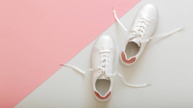 Uçan bağcıklı beyaz spor ayakkabılar, pembe arka planda bağcıklı kadın beyaz deri ayakkabılar. Bir çift şık spor ayakkabısı rahat spor giyim hipster kadın ayakkabısı. Üst görünüm uzun web pankartı kopyalama alanı.