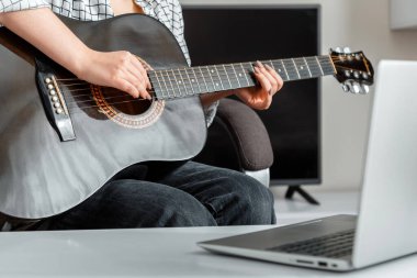Çevrimiçi gitar performansı. Genç bir kadın dizüstü bilgisayarında online izleyicilere akustik gitar çalıyor. Kilitleme sırasında video konseri veya çevrimiçi dersler gitar eğitimi müziği ve eğitim.