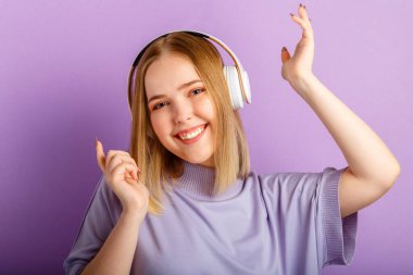 Kulaklıklı dansçı kadın. Aktif neşeli kadın kulaklıkla müzik dinlerken. Genç kız mor arka planda izole edilmiş eğlence kulübünde eğleniyor..