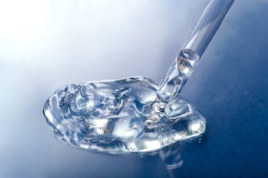 Mavi renkli cam arka planda pipeti olan şeffaf jel serumu örneği. Cilt bakımı ya da tıbbi sıvı jel için kozmetik ürün