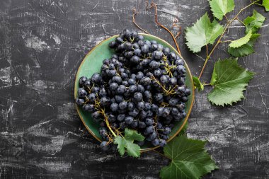 Tabakta siyah üzümler ve koyu masa manzaralı asma bitkisi. Tatlı sulu üzümler siyah beton zemin üzerinde besin düz yatıyordu.