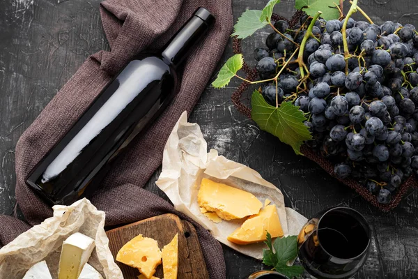 赤ワインボトル別のチーズブドウ。ヴィンテージはまだカマンベール熟成チーズ、ブドウとワインの組成物を生きます。ワインを飲むモックアップ。レストランディナー、暗いコンクリートの背景にワインの試飲 — ストック写真
