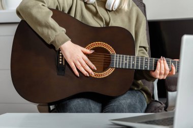 Çevrimiçi dersler gitar eğitimi müzik eğitimi ve tecrit sırasında eğitim. Çevrimiçi gitar performansı. Genç bir kadın dizüstü bilgisayarında online izleyicilere akustik gitar çalıyor..