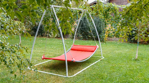 Hammock swing in metal frame with nobody on green lawn in backyard near house cottage. Rest relax relaxation alone on Red hammock swing in Summer garden. Long web banner
