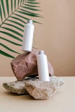 Doğal güzellik kozmetik şişeleri taş kaide bej arka planda palmiye yaprakları ile cilt için beyaz makyaj ürünleri. Doğal cilt bakım losyonu şişeleri havada asılı duran beyaz kozmetik şişeleri..
