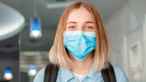 Happy smiling woman Schoolgirl in blue protective mask with backpack. Young woman student in medical mask. Portrait of blonde female student Girl at university interior during lockdow. Long web banner