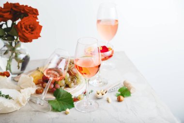 Üzüm peyniriyle beyaz masada farklı şarap kadehlerinde gül şarabı, bir buket çiçek. açık gri beton zemin üzerinde gül şarabı kompozisyonu.