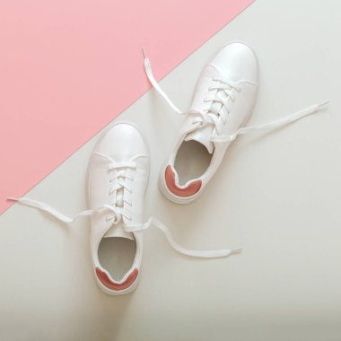 Uçan bağcıklı beyaz spor ayakkabılar, pembe arka planda bağcıklı kadın beyaz deri ayakkabılar. Bir çift şık spor ayakkabısı rahat spor giyim hipster kadın ayakkabısı. Üst görünüm