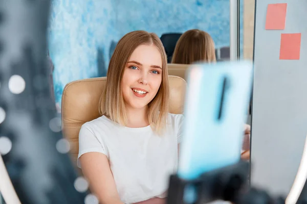 Young woman blogger records live video content, broadcasts live to subscribers using mobile phone and ring light lamp. Vlogger ternager girl smiles and speaks to camera. — Stock Photo, Image