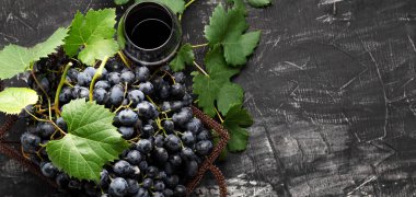 Siyah üzüm sepeti ve koyu kırsal beton arka planda bir bardak kırmızı şarap. Düz şarap kompozisyonu kırmızı şarap bardağı ya da üzüm suyu siyah taş masaya serilmişti. Uzun web pankartı kopyalama alanı