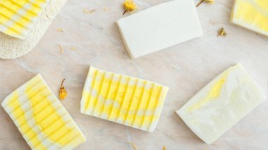 Doğal zeytinli sabun kalıpları, otlar, kuru kadife çiçekleri. Birçok beyaz ev yapımı sabun, vücut bakımı için spa banyosu ürünleri. Hijyen malzemeleri mermer masada. Uzun web pankartı