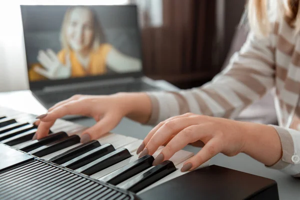 Woman playing piano during video call via laptop. Female hands musician pianist improves skills playing piano online classes with teacher. Online Music education