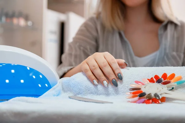 Mujer con uñas acrílicas artificiales recoge nuevo color de esmalte durante el procedimiento de manicura. Proceso de manicura en salón de belleza. Higiene belleza de las manos en salón de uñas. — Foto de Stock