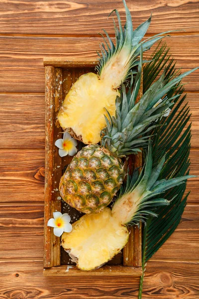 Piña madura. Mitades de piña de frutas tropicales de verano y piña entera sobre mesa oscura marrón en caja de madera con flores de plumería tropical. Vista superior — Foto de Stock