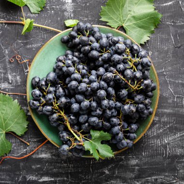 Tabakta siyah üzümler ve koyu masa manzaralı asma bitkisi. Tatlı sulu üzümler siyah beton zemin üzerinde besin düz yatıyordu kare