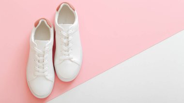 Beyaz spor ayakkabılar, pembe arka planda bağcıkları olan kadın beyaz deri ayakkabılar. Bir çift şık spor ayakkabısı rahat spor giyim hipster kadın ayakkabısı. Üst görünüm uzun web pankartı kopyalama alanı