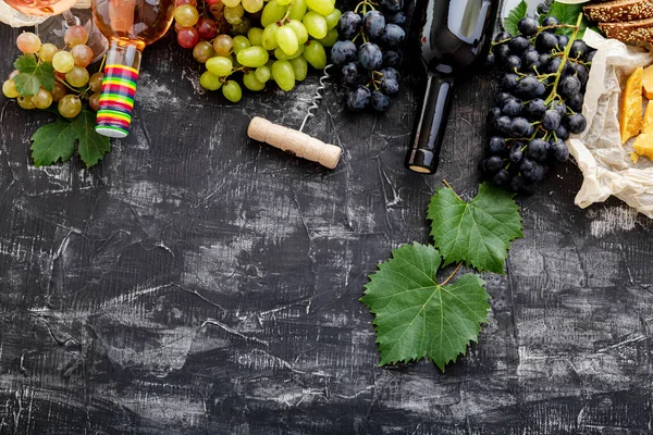 Rose red wine in bottles cheese, white pink and black grapes with vine plant on dark concrete background. Assortment different types of wine and grape grade varieties. Food drink frame