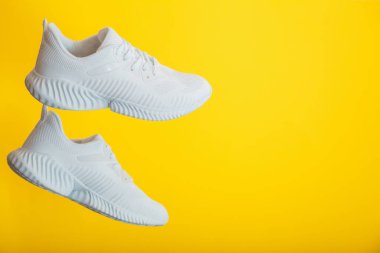 Beyaz spor ayakkabılar sarı arka planda uçar. Renk duvarında fotokopi alanı olan bir çift modern spor erkek spor ayakkabısı..