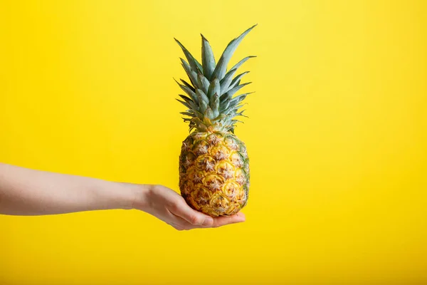 Piña en mano femenina. Fruta tropical madura de piña jugosa aislada sobre fondo de color amarillo. Concepto minimalista de verano. — Foto de Stock