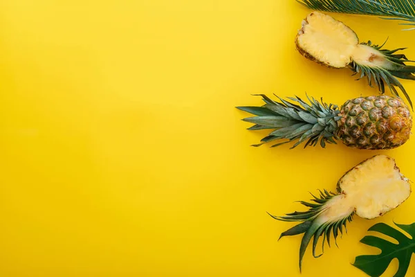 Piñas y hojas de palma sobre fondo veraniego de color amarillo. Frutas enteras de piñas tropicales de verano y mitades de piña en rodajas — Foto de Stock
