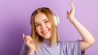 Kulaklıklı dansçı kadın. Aktif neşeli kadın kulaklıkla müzik dinlerken. Genç kız mor arka planda izole edilmiş eğlence kulübünde eğleniyor. Uzun web pankartı