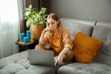 Güzel genç bayan alışverişçi evdeki kanepede otururken dizüstü bilgisayar ve kredi kartı kullanarak online alışveriş yapıyor. Kadınlar online alışverişleri düşünceli bir şekilde yaparlar. Düşünceli ve düşünceli bir alıcı.