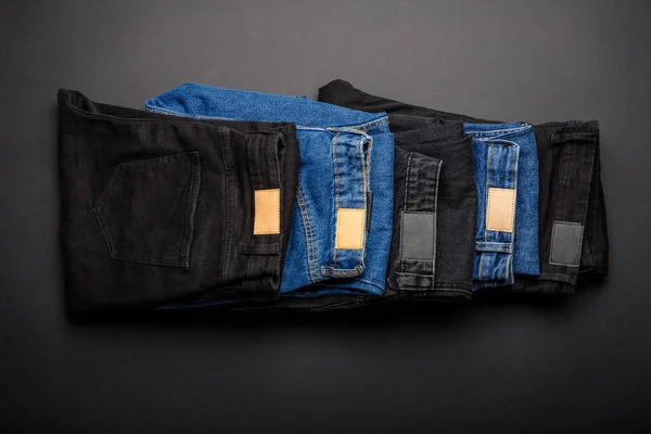 Denim modré džíny a černé džíny naskládané v hromadě na černém pozadí Top View. Denim džínové kalhoty oblečení složené v zásobníku. — Stock fotografie