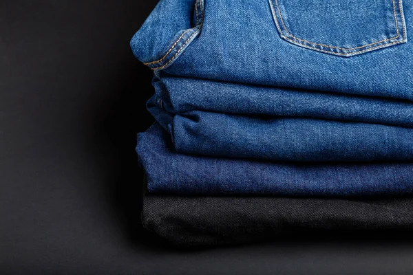 Blue jeans trousers stack. Stack of blue jeans on black background with copy space. — Stock Photo, Image