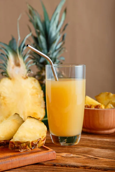 Pineapple juice in glass. Glass of fresh natural pineapple juice cocktail with metal reusable tube on brown wooden table with ingredients. Raw pineapple sliced fruit.