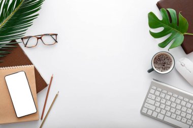 Bilgisayar klavyesi ve ofis malzemeleriyle modern çalışma alanı. Tropikal palmiye yaprakları olan boş bir cep telefonu modeli. Çerçeve Düz
