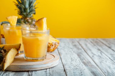 Lezzetli ananas suyu ve beyaz ahşap masa ve sarı yaz arkaplanlı malzemeler. Taze doğal ananas suyu kokteyli ve fotokopi alanı olan meyve suyu bardağı.