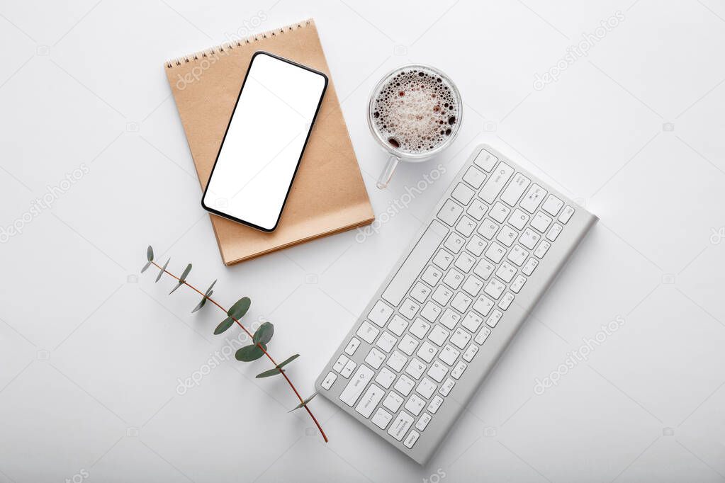 Smartphone mock up with note keyboard coffee cup green plant on white work space desk. Top view flat lay. Mobile phone on modern office desk workspace.