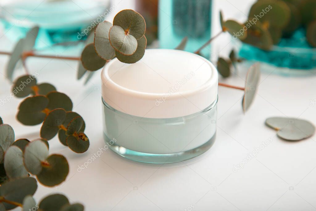 Moisturizing cream in glass jar with eucalyptus leaves. Set of eucalyptus skin care cosmetics in white mockup packaging on white background. Natural skincare cosmetics or medical eucalyptus ointment
