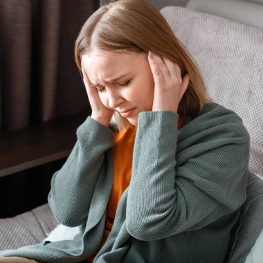 Ciddi migren ağrısı olan üzgün bir kadın tapınakları elleriyle tutuyor. Kadının ateşi ve baş ağrısı evde tek başına oturuyor. Yakın çekim kare portresi