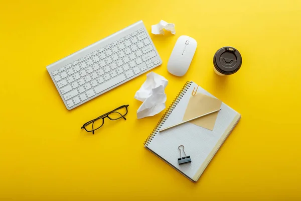 Work space desk layout with note keyboard coffee cup glasses bright color yellow background. Modern office desk work space flat lay composition. White stationery on home office workplace pc computer.
