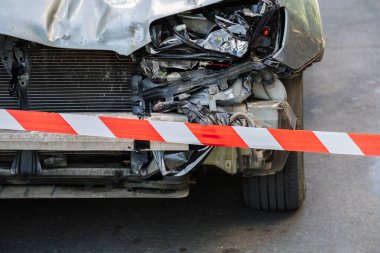 Trafik kazasının önünde kırmızı beyaz uyarı şeridini geçti. Kırık bir arabanın kaputu kırmızı uyarı bandıyla çevrili. Kırık Çarpıcı ve Işıklı Araba Farları Yol yüzeyinde asfalt Kimse olmadan