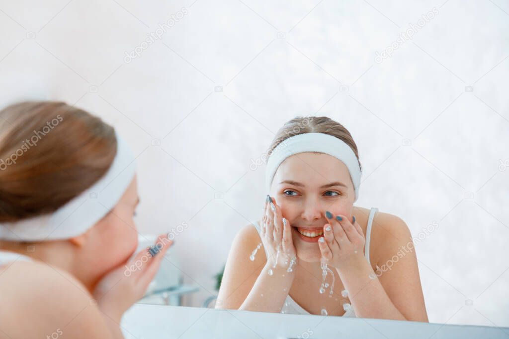 Young blonde woman washes face pure water in bathroom sink. Teen girl cleanse face skin. Self Care morning routine woman portrait reflection in mirror. Dauly face hygiene.