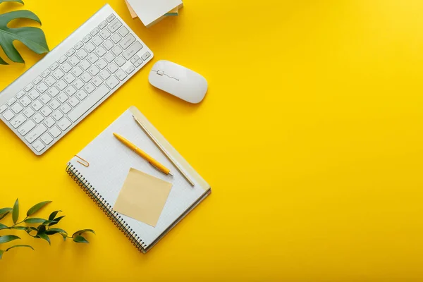 Office desk workspace on bright color yellow background. Office table Work space layout with computer keyboard, plant mouse notepad notes and copy space. Top view office table with palm plant.