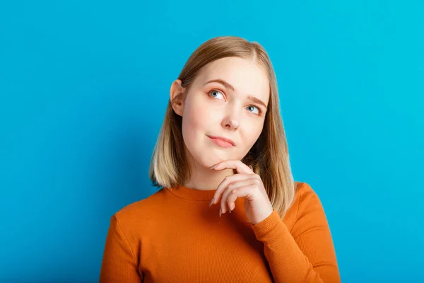 Young woman think thought. Portrait of emotional teenager girl looking on empty space deep thinking about idea or question isolated on color blue background with copy space.