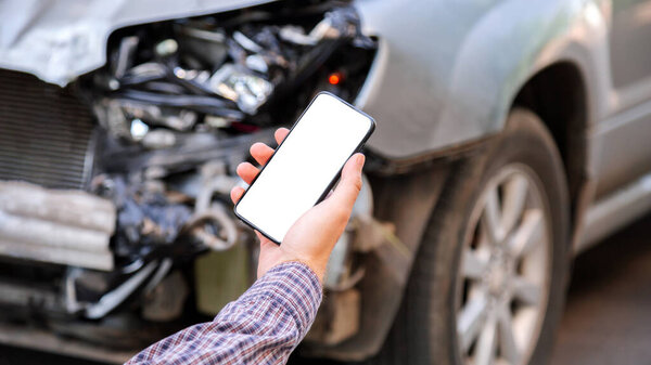 Мужчина держит в руках макет мобильного белого экрана телефона после автомобильной аварии. Звонок в страховую службу в веб-приложении на место аварии. Смартфон перед разбитой машиной. Длинный веб-баннер.