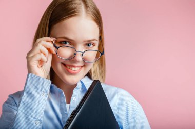 Gözlüklü gülümseyen genç bir kadının duygusal portresini kapat. Dizüstü bilgisayarlı. Fotokopi çekilen pembe arka planda izole edilmiş. Genç kız öğrenci ya da bilgisayarlı ofis çalışanı.
