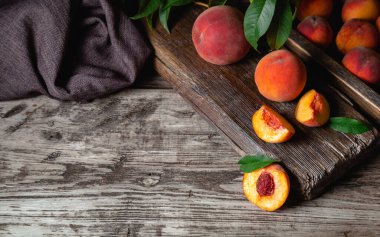 Fotokopi alanı olan koyu ahşap bir masada sulu olgun şeftaliler. Lezzetli çiftlik şeftalileri, yaprakları yarım kalmış meyveler, kemikli şeftali. Durgun şeftali rengi karanlık anahtar.