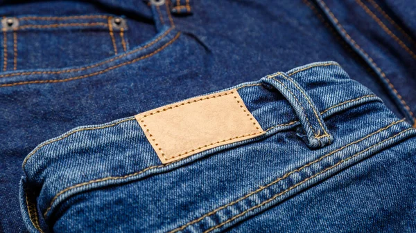 Blue denim jeans with emty label. Brown blank leather label tag on denim pants background. Blank mockup beige leather label. Close up long web banner — Stock Photo, Image