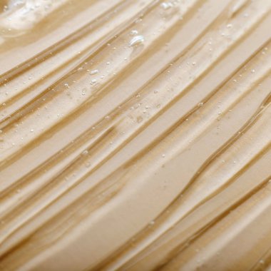 Bej rengi açık renk arka planda kozmetik nemlendirici ürünün berrak sulu jel dokusu. Hyaluronik asit jeli ya da deri tonunda kolajen arkaplan dokusu. Serum yüzeyi. Meydanı kapatın.