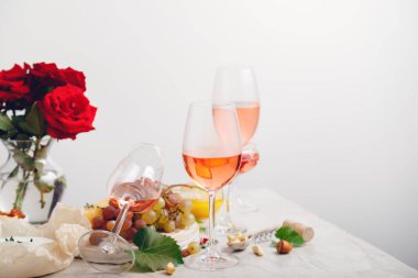 Gül şarabı ve yaz, parti etkinliğinde çiçeklerle süslenmiş şenlik masasında üzümlü pembe kokteyller içerler. Pembe şarap kadehleri kopyalama alanı olan minimal yerleşim.