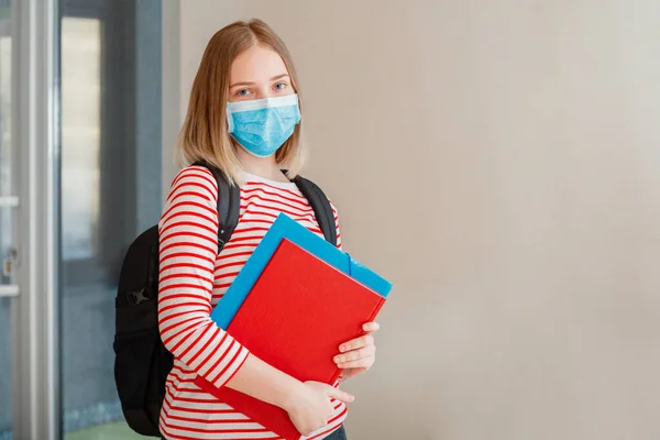 Jovem estudante em máscara médica protetora. Retrato de estudante loira Menina no interior da universidade durante coronavírus covid 19 lockdown com espaço de cópia — Fotografia de Stock