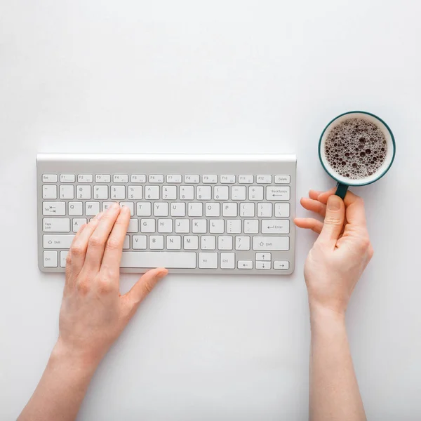 Woman typing on computer keyboard and drinking coffee at workplace. office desktop workspace with female hands on white background.